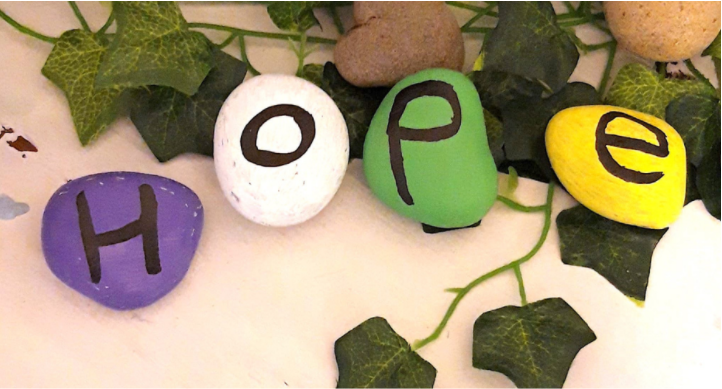 Four pebbles painted in different colours with letters spelling out HOPE