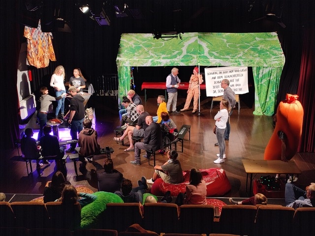 A large group of people on a theatre stage with props and costumes